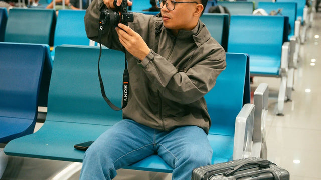 Traveler checking a camera in an airport terminal with carry-on luggage – best camera backpacks for mirrorless travel 2026