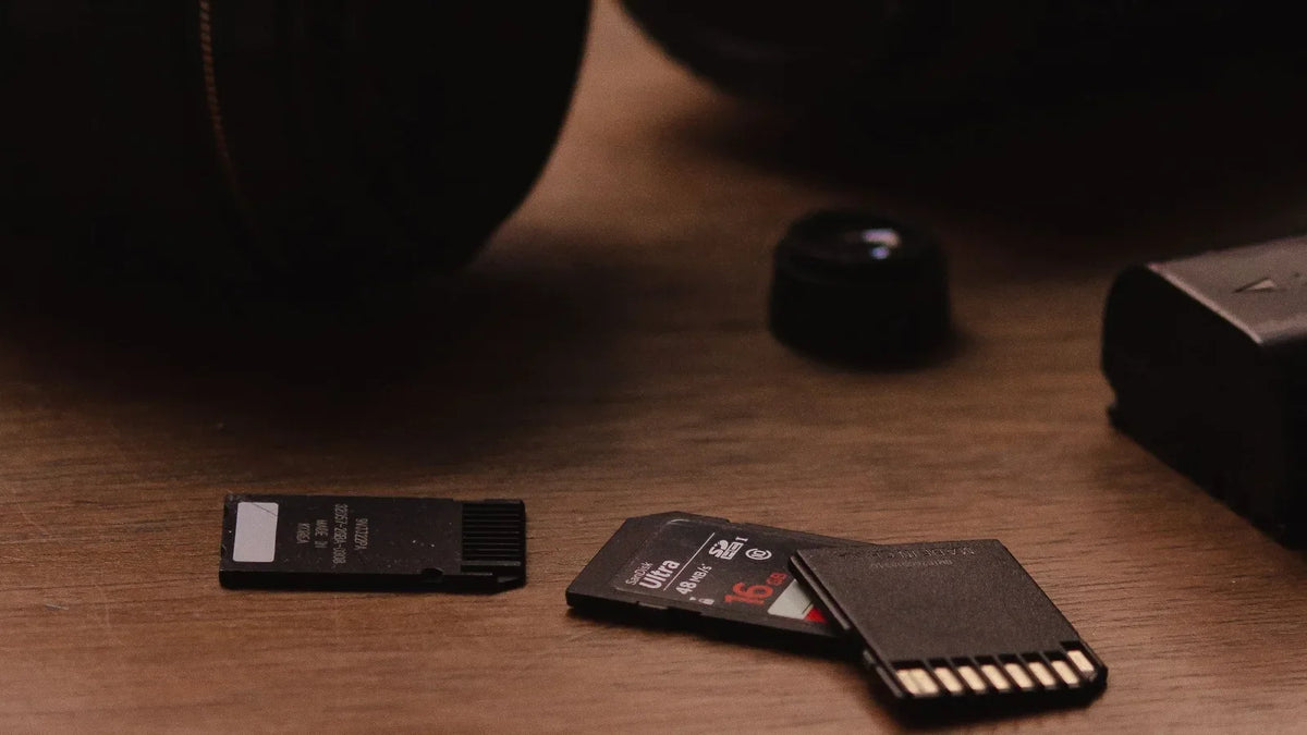 SD memory cards next to camera lenses on a wooden table – best SD card for Insta360 X5, Sony and Canon